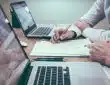 person holding pencil near laptop computer